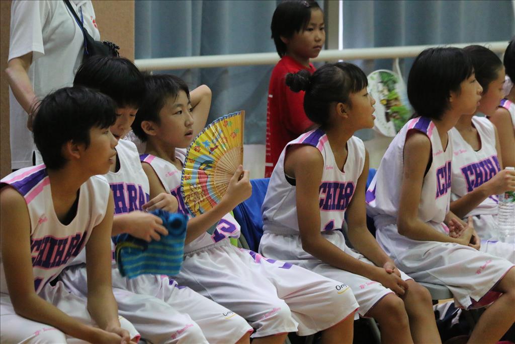日本小球員在炎熱夏天的臺灣打球，除了手中的摺扇外，背後還有小球員的稚齡妹妹主動打扇子為學姊們祛暑氣。