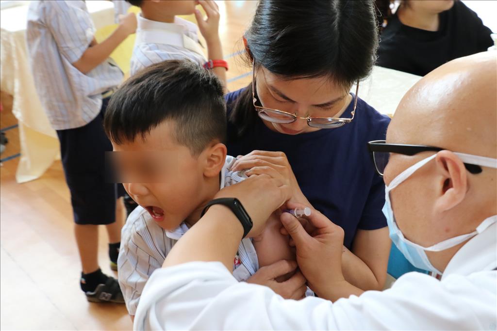 低年級小朋友懼怕打針，需要老師抱著注射疫苗。